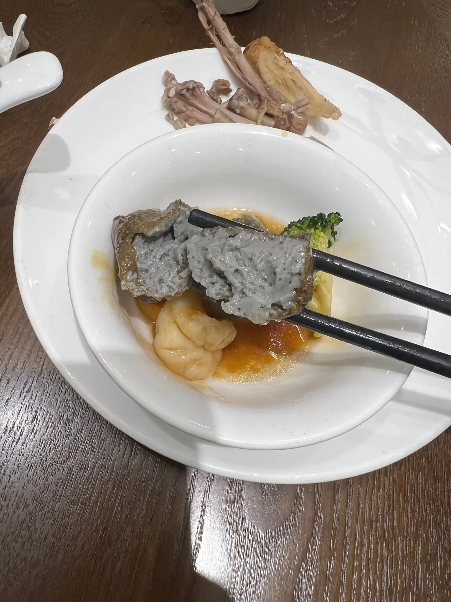 A piece of black sesame tofu held in chopsticks