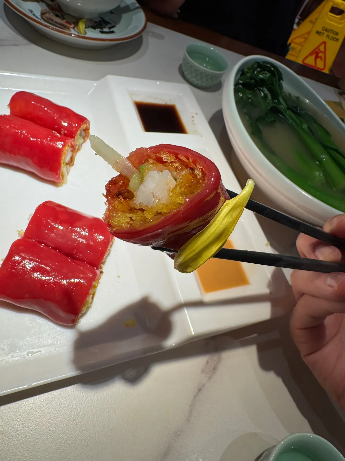 A red rice roll held in chopsticks, showing the filling