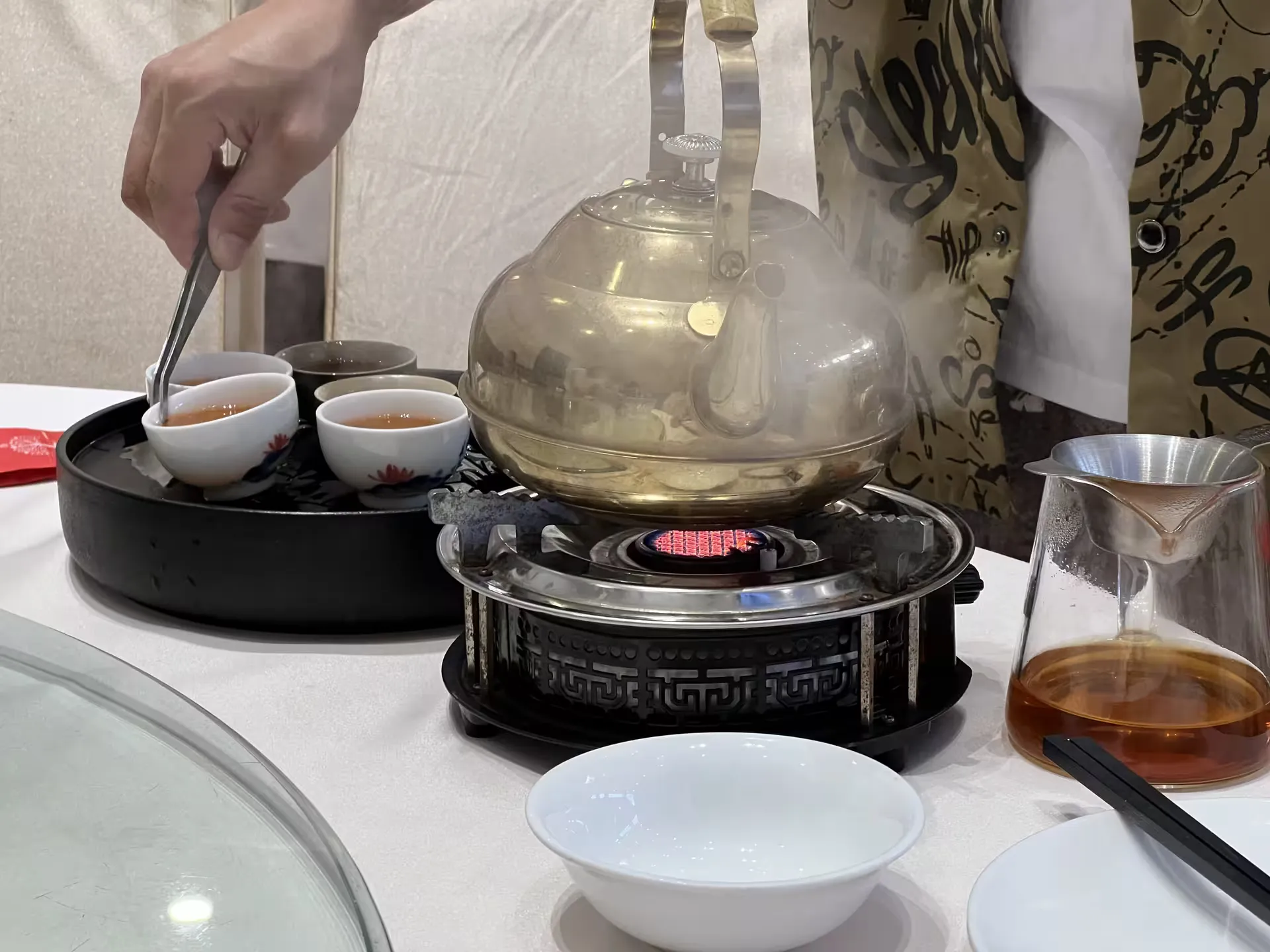 Holding a teacup with small tongs to rinse it in hot water